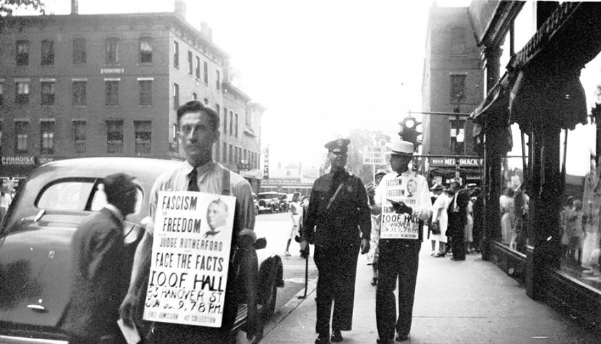 The Witnesses' signs show a portrait of their leader Joseph "Judge" Rutherford, who made many of the recordings played by Witnesses during their proselytizing.